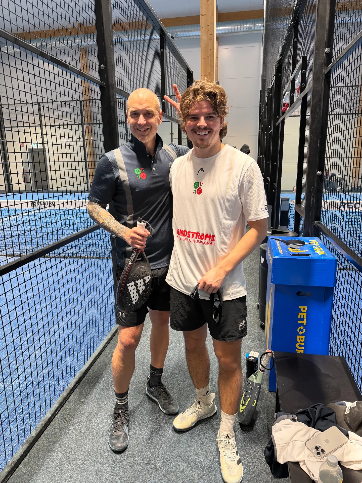 Två leende padelspelare intill banorna i Bålsta Padel Club